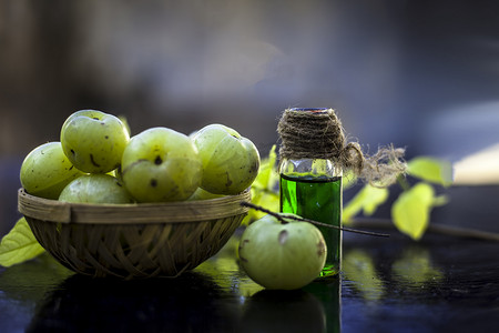 印度醋栗的特写镜头，其提取的精华或浓缩在木质表面的透明瓶中，水果和蔬菜篮中装有生醋栗。