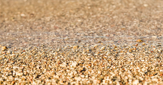 沙滩上的沙子、小鹅卵石和流动的波浪背景。