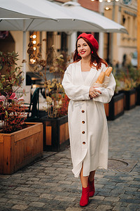 一位身穿红色贝雷帽和白色开衫的漂亮女人的画像，她手里拿着长棍面包，漫步在秋天的城市