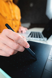 随便的人，自由职业者用手写笔在数字平板电脑屏幕上书写，在办公桌上的笔记本电脑上工作。