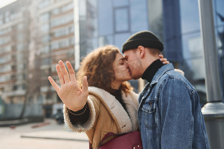 在商业大楼附近的城市里，一对穿着休闲保暖衣服的快乐情侣在户外接吻
