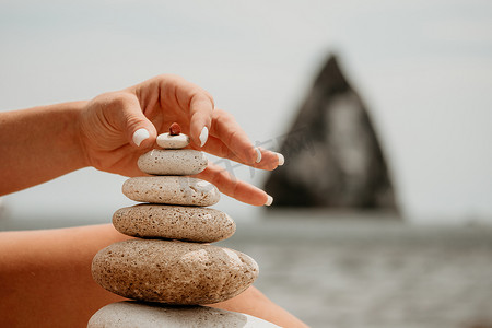 石子摄影照片_女人 bilds 石头金字塔在海边在一个阳光明媚的日子在蓝色的大海背景。