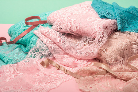 粉红色背景中用于内衣、内裤和胸罩的一堆颜色丰富的亮蕾丝