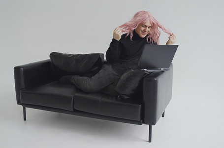 一个戴着粉色假发的男人坐在沙发上，通过笔记本电脑上的视频链接进行交流。