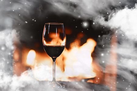 大气冬季背景摄影照片_冬季气氛和圣诞假期，壁炉前的一杯葡萄酒，窗玻璃上覆盖着雪花，假期背景