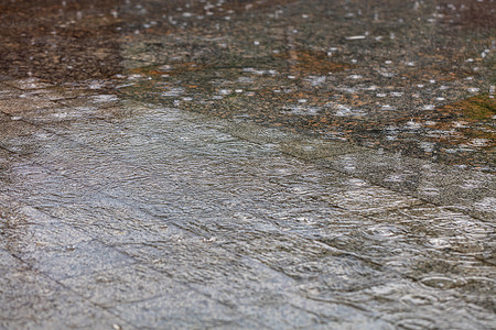 雨中水面上的同心圆覆盖了城市人行道的花岗岩区域。
