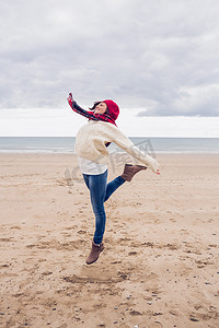 穿着时尚保暖衣服的女人在海滩上跳跃