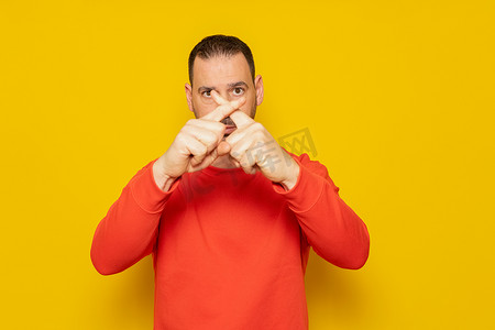 黄色手指手势摄影照片_黄色背景下留着胡子的西班牙裔男子表示拒绝，手指交叉做出拒绝手势，他对当局在气候变化问题上的无能感到愤怒。