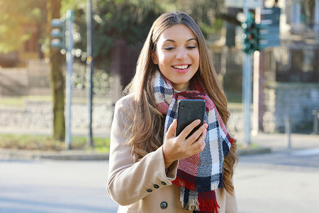 年轻微笑的大学生女孩在城市街道上用智能手机给朋友打电话