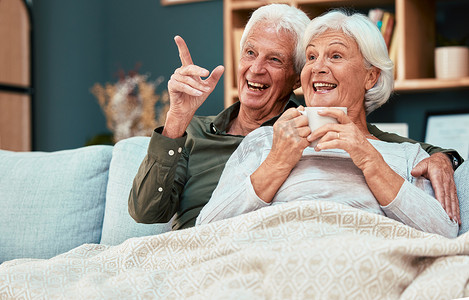 退休夫妇，老人，在家里的沙发上看电视，看有趣的电视节目或电影放松身心，享受幸福和咖啡。