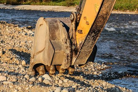 石子摄影照片_挖掘机（挖掘机）铲斗在河边挖石头。