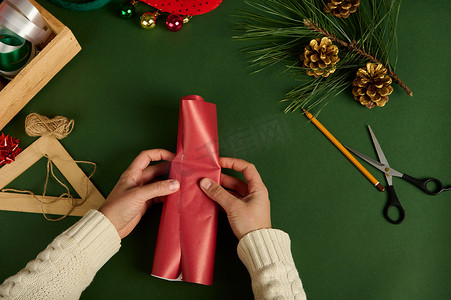 特写 Top view 女人用红纸在绿色背景上用包装材料包装一份小礼物。 