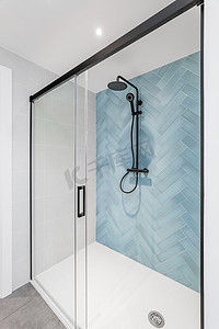 带玻璃淋浴间的白色浴室，墙壁上装饰着淡蓝色的人字形瓷砖。