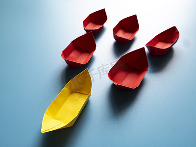 领先摄影照片_领导概念-黄色纸船折纸在蓝色封面背景上领先其余的红纸船。