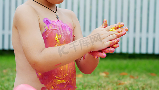 小孩梦想摄影照片_一个小孩，一个四岁的男孩在玩耍，用手指画画，装饰自己，在花园里，坐在毯子上，在草地上，草坪上，在夏天。