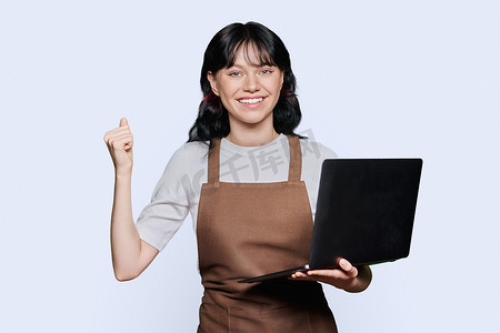 穿着围裙的快乐年轻女服务员看着笔记本电脑屏幕