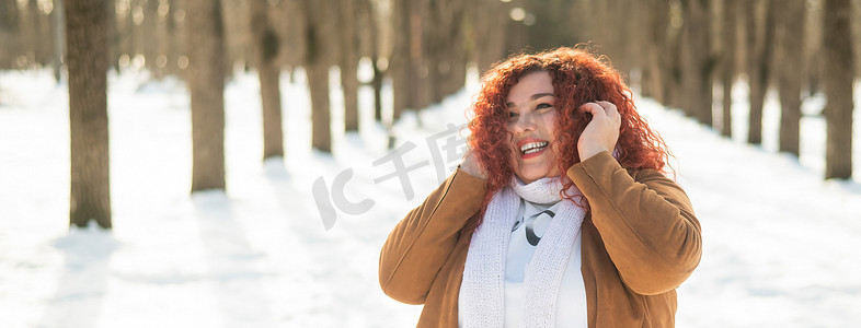 一个丰满的女人冬天在公园散步时戴着耳机听音乐。