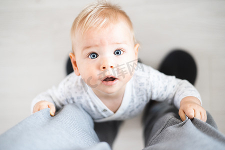 从上到下看快乐的男婴在家里抱着父亲的运动裤迈出第一步。