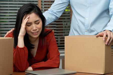 悲伤的亚洲女人在被裁员和失业后，把​​东西装在纸箱里，在办公室的桌子上哭泣。