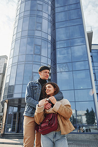 一对穿着休闲保暖衣服的快乐夫妇在商业大楼附近的城市户外散步