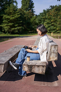 亚洲女孩，在公园里画画，在阳光明媚的日子里坐在街上，拿着数字图形平板电脑和笔，开心地笑着