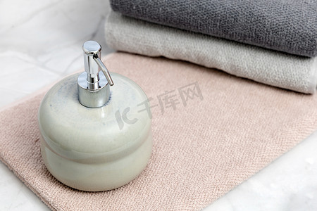 白色大理石背景上的陶瓷皂液器和折叠毛巾。