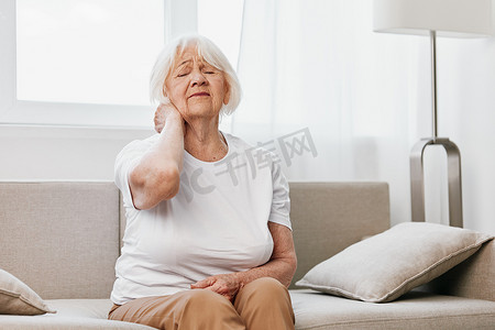 房屋质量摄影照片_老年妇女坐在沙发上颈部严重疼痛，晚年健康问题，生活质量差。