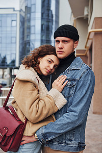 在商业大楼附近的城市里，一对穿着休闲保暖衣服的快乐夫妇在户外互相拥抱