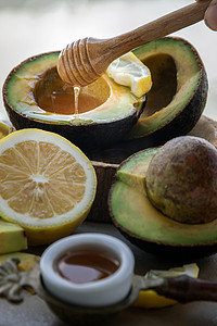 蜂蜜柠檬摄影照片_蜂蜜从木棒滴头滴入切成两半的新鲜有机鳄梨和蜂蜜柠檬片的特写镜头。