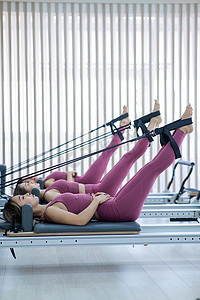 三名身穿粉色运动服的亚洲女性在塑身床上做普拉提运动。