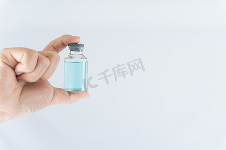 疫苗瓶摄影照片_女医生或科学家戴着医用口罩并拿着药液疫苗瓶的特写手。 