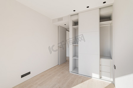 空卧室摄影照片_空荡荡的干净明亮的卧室配有浅色木镶木地板和带推拉门的白色衣柜。