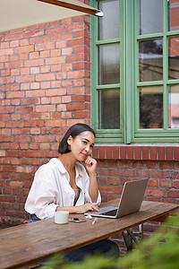 坐在户外使用笔记本电脑、在线聊天、在办公室外使用电脑的黑发美女