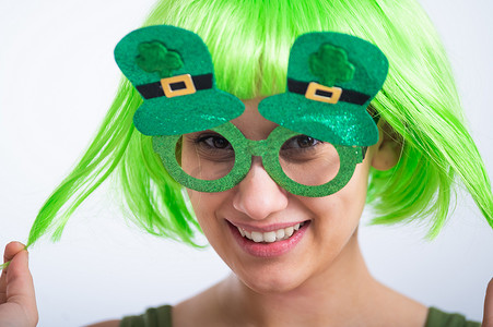 假发摄影照片_戴着绿色假发和滑稽眼镜的快乐年轻女性在白色背景下庆祝圣帕特里克节