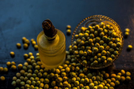 在黑色表面的玻璃瓶中拍摄一碗绿豌豆及其提取的油。