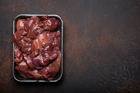 生鸡肝在黑色超市托盘顶部视图在深色乡村混凝土背景厨房桌子上。