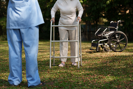 亚洲老年妇女与护士一起练习用铝制助行器走路以确保安全。