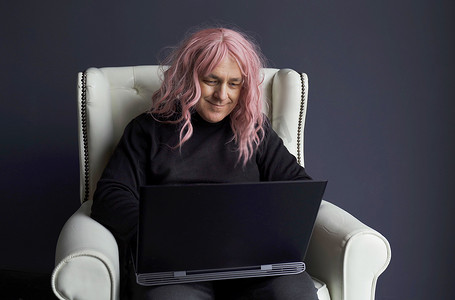一个戴粉色假发的男人坐在白色椅子上，在电脑前工作
