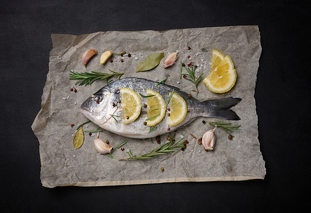 全鱼摄影照片_棕色羊皮纸上的生全多拉多鱼和烹饪香料，黑桌上的顶视图