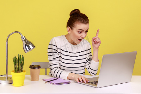女人看起来对天才的想法感到惊讶，在笔记本电脑上工作时举起手指受到启发。