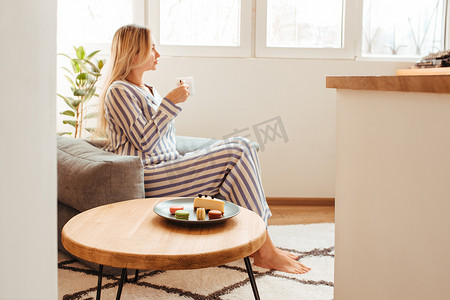 一个穿着睡衣的女人早上在桌边喝咖啡，吃糖果芝士蛋糕甜通心粉。