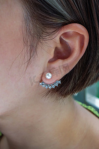 银耳环摄影照片_戴着漂亮的银耳环、白色珍珠和钻石的年轻女子的细节。