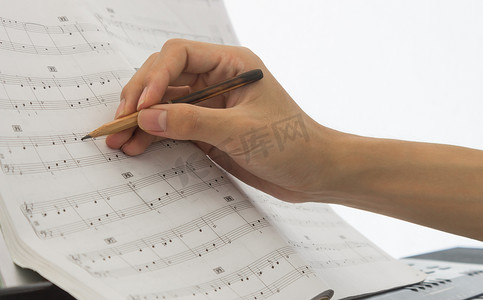 钢琴演奏者的手正在钢琴乐谱或乐谱上写笔记