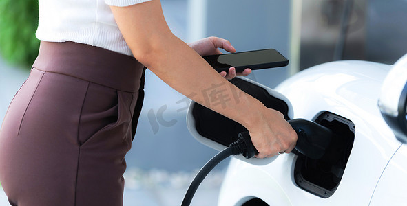 特写进步女性在家庭充电站为她的 EV 汽车充电。