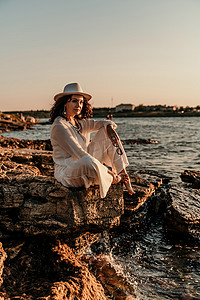 裤装摄影照片_一位穿着白色裤装和帽子的女人站在沙滩上享受大海。
