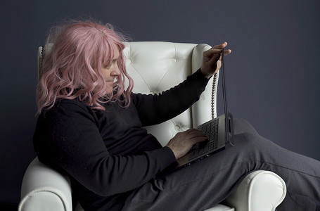 假发摄影照片_一个戴着粉色假发的男人坐在椅子上，通过视频链接进行交流。