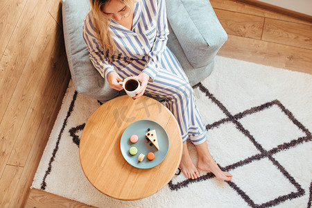 一个穿着睡衣的女人早上在桌边喝咖啡，吃糖果芝士蛋糕甜通心粉。