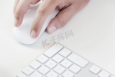 男性手点击白色鼠标，右侧有白色键盘。