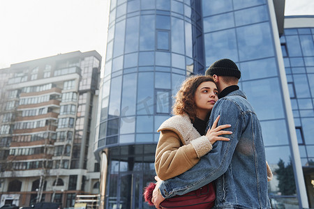 保暖衣服摄影照片_一对穿着休闲保暖衣服的快乐夫妇在商业大楼附近的城市户外散步