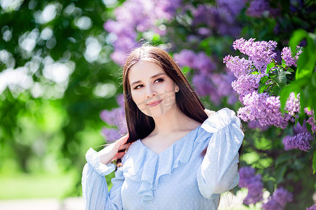 长头发的漂亮女孩站在花园里，开着淡紫色的花